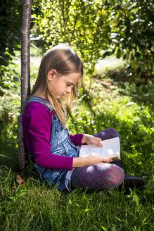 Kleines Mädchen sitzt auf einer Wiese im Garten und liest ein Buch - SARF002110