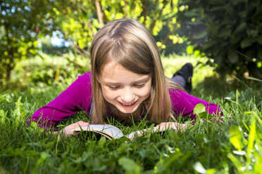 Little girl lying on a meadow in the garden reading a book - SARF002113