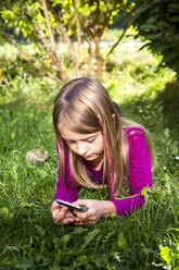 Little girl lying on a meadow in the garden looking at smartphone - SARF002118