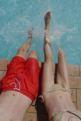 Italien, Bruder und Schwester sitzen am Rande eines Swimmingpools und spritzen Wasser - LBF001212