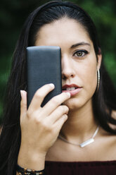 Young woman covering one eye with smartphone - JRFF000079