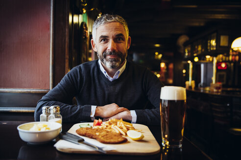 Smiling man in restaurant having Wiener Schnitzel with French fries - AIF000093