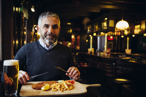 Smiling man in restaurant having Wiener Schnitzel with French fries stock photo