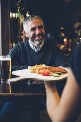 Lächelnder Mann im Restaurant, der Wiener Schnitzel mit Pommes frites erhält - AIF000097