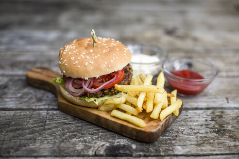 Homemade burger with lettuce, meat, tomato, onion and french fries on chopping board - SARF002137
