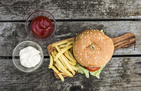 Homemade burger with lettuce, meat, tomato, onion and french fries on chopping board stock photo