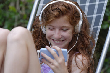 Glückliches Mädchen, das mit Kopfhörern Musik hört und auf sein Smartphone schaut - LBF001214