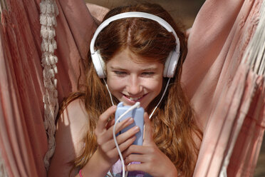 Porträt eines Mädchens mit Kopfhörern und Smartphone in einer Hängematte - LBF001216