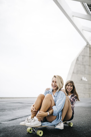 Zwei junge Frauen fahren auf einem Longboard, lizenzfreies Stockfoto