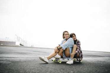 Zwei junge Frauen sitzen auf einem Longboard - JRFF000099