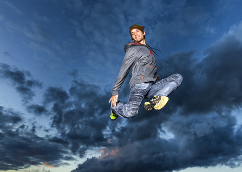 Junger Mann springt in die Luft vor dem Abendhimmel, lizenzfreies Stockfoto