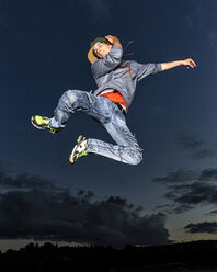 Young man jumping in the air in front of evening sky - STSF000940