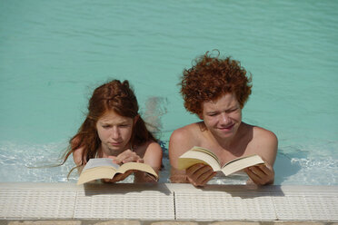 Rothaariges Mädchen und Junge liegen nebeneinander in einem Schwimmbad und lesen ein Buch - LBF001221