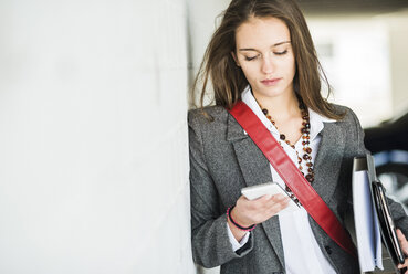 Young woman holding folder looking at cell phone - UUF005749