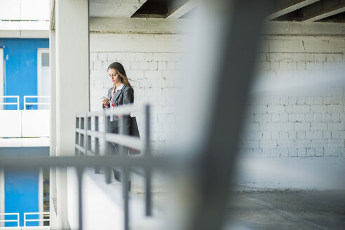 Junge Frau in einem Parkhaus, die einen Ordner hält und auf ihr Handy schaut - UUF005761