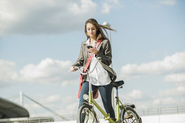 Junge Frau mit Fahrrad schaut auf ihr Handy - UUF005768