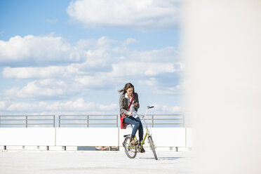 Junge Frau auf dem Fahrrad schaut auf ihr Handy - UUF005773
