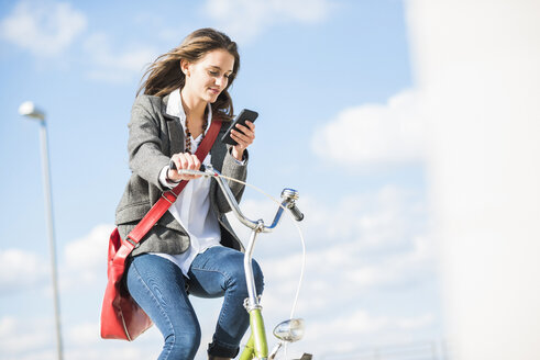 Junge Frau auf dem Fahrrad schaut auf ihr Handy - UUF005774