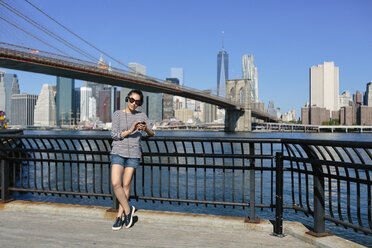 USA, New York City, portrait of young woman hearing music with headphones in front of skyline - GIOF000132