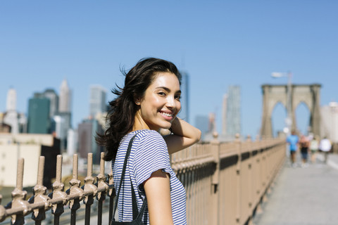 USA, New York City, Porträt einer lächelnden jungen Frau auf der Brooklyn Bridge, lizenzfreies Stockfoto