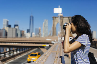 USA, New York City, young woman standing on Brooklyn Bridge taking a photo with camera - GIOF000135
