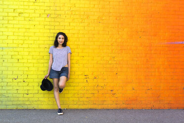 Porträt einer lächelnden jungen Frau, die sich an eine gelbe Backsteinmauer lehnt - GIOF000141
