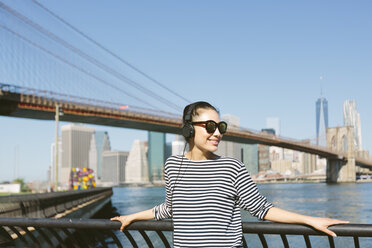 USA, New York City, portrait of young woman hearing music with headphones in front of the skyline - GIOF000146