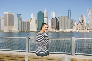 USA, New York City, junge Frau sitzt vor der Skyline und schaut über ihre Schulter - GIOF000152