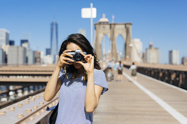 USA, New York City, junge Frau steht auf der Brooklyn Bridge und macht ein Foto mit Kamera - GIOF000154