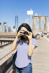 USA, New York City, junge Frau steht auf der Brooklyn Bridge und macht ein Foto mit Kamera - GIOF000158