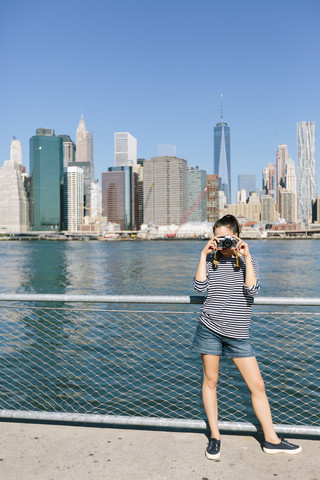 USA, New York City, junge Frau beim Fotografieren mit Kamera vor der Skyline, lizenzfreies Stockfoto