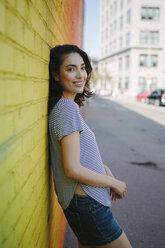 Porträt einer lächelnden jungen Frau, die sich an eine gelbe Backsteinmauer lehnt - GIOF000164