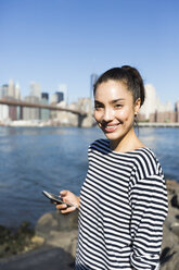 USA, New York City, portrait of smiling young woman with smartphone - GIOF000168