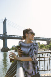 USA, New York City, lächelnde junge Frau mit Softdrink, die auf ihr Smartphone schaut - GIOF000169