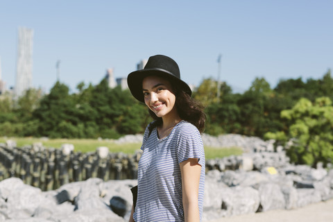USA, New York City, Porträt einer lächelnden jungen Frau mit schwarzem Hut, lizenzfreies Stockfoto