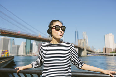 USA, New York City, portrait of young woman with headphones and sunglasses in front of skyline - GIOF000173