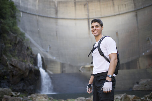 Lächelnder Ultra-Trail-Läufer mit einem Staudamm im Hintergrund - RAEF000517