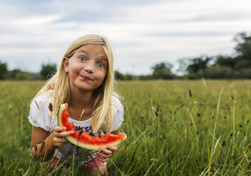 Girl with slice of watermelon standing on a meadow making a face - MGOF000800