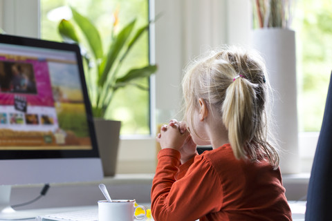 Kleines Mädchen beobachtet etwas auf dem Computerbildschirm, lizenzfreies Stockfoto