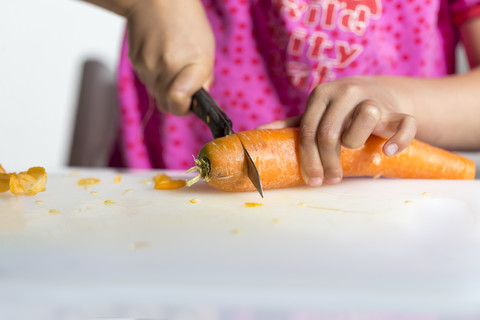 Hände eines kleinen Mädchens, das Karotten schneidet, lizenzfreies Stockfoto