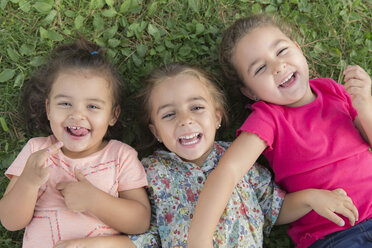 Porträt von drei lachenden kleinen Mädchen, die nebeneinander auf einer Wiese liegen - ERLF000054