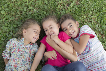 Porträt von drei lachenden Kindern, die nebeneinander auf einer Wiese liegen - ERLF000056
