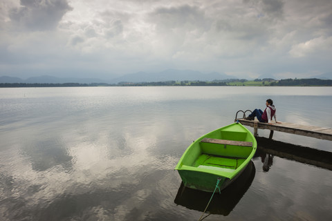 Frau auf Steg sitzend, Hopfensee, grünes Ruderboot, lizenzfreies Stockfoto