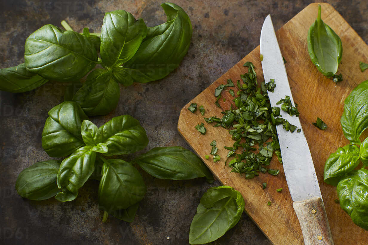 Whole and chopped basil leaves and kitchen knife on wooden board