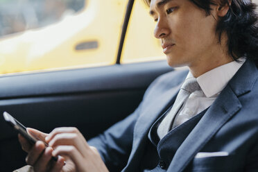 Businessman on back seat of car using cell phone - GIOF000213