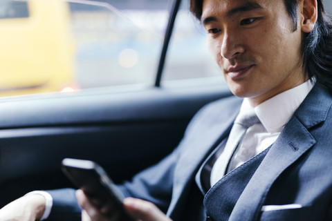 Lächelnder Geschäftsmann auf dem Rücksitz eines Autos, der ein Mobiltelefon benutzt, lizenzfreies Stockfoto