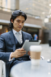 USA, New York City, Geschäftsmann in einem Straßencafé mit Blick auf ein digitales Tablet - GIOF000230