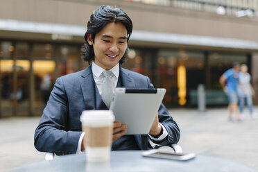 USA, New York City, lächelnder Geschäftsmann in einem Straßencafé mit Blick auf ein digitales Tablet - GIOF000235