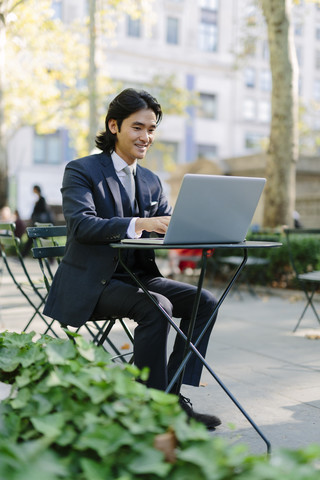 USA, New York City, Manhattan, lächelnder Geschäftsmann bei der Arbeit mit einem Laptop im Bryant Park, lizenzfreies Stockfoto