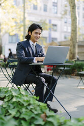 USA, New York City, Manhattan, lächelnder Geschäftsmann bei der Arbeit mit einem Laptop im Bryant Park - GIOF000247